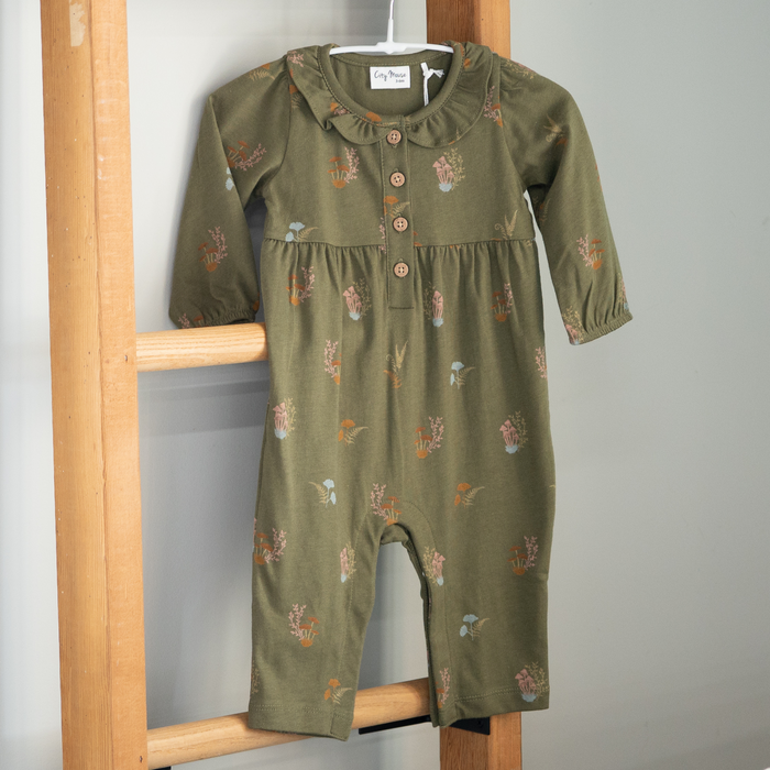 Green baby romper with floral patterns on a wooden hanger against a gray wall.