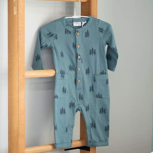 Blue baby romper with tree pattern hanging on a wooden rack against a gray wall.