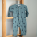 Blue baby romper with tree pattern hanging on a wooden rack against a gray wall.