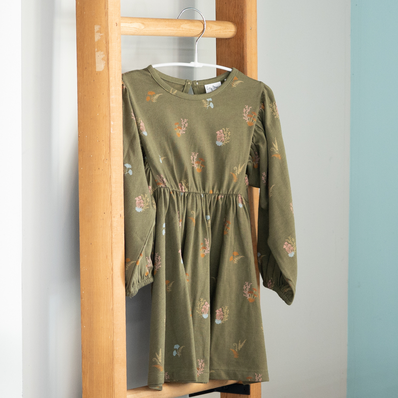 Green dress with floral patterns on a wooden hanger against a light gray wall.