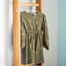Green dress with floral patterns on a wooden hanger against a light gray wall.