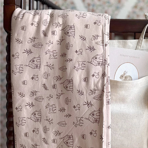 Pink Do.Re.Mi. print blanket draped over the side of a wooden crib, showing the soft quilted texture and whimsical musical pattern.