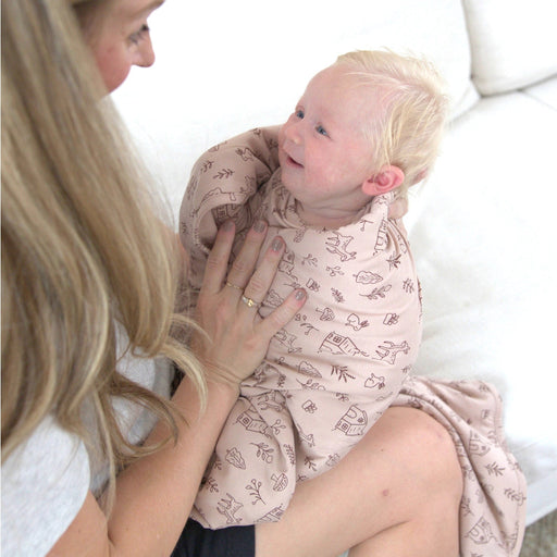 A mother sits on a bed holding a toddler wrapped in the Do.Re.Mi. Cloud Blanket, highlighting its plush thickness and gentle drape.
