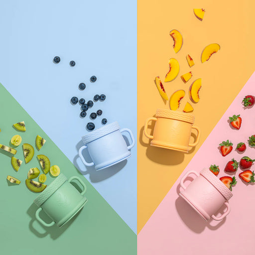 Three Coastal Cups in pink, blue, and sage green arranged on colorful pastel quadrants with snacks like blueberries, bananas, and strawberries scattered around.