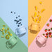 Three Coastal Cups in pink, blue, and sage green arranged on colorful pastel quadrants with snacks like blueberries, bananas, and strawberries scattered around.