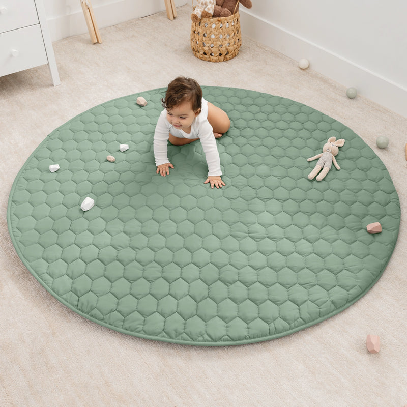 Child crawling on a green round mat in a room with toys scattered around