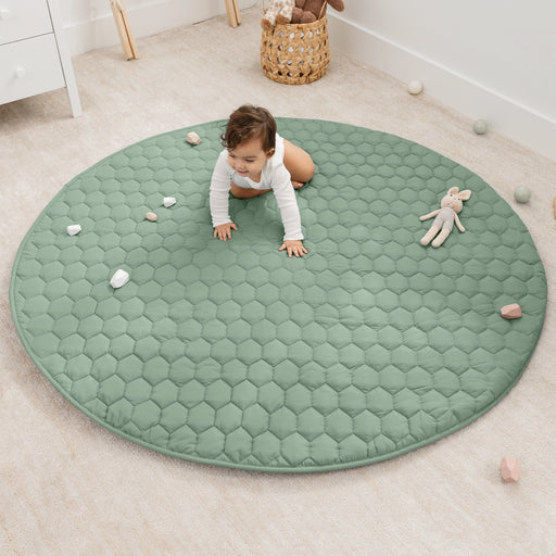 Child crawling on a green round mat in a room with toys scattered around