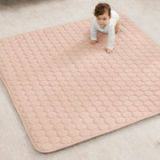 Baby on a quilted mat on a light-colored floor