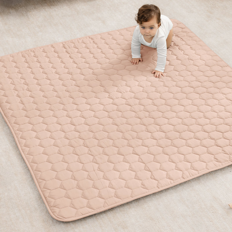 Baby on a quilted mat on a light-colored floor