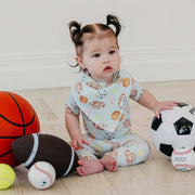 Baby sitting among sports balls wearing the sports ball print Copper Pearl All Star bandana bib