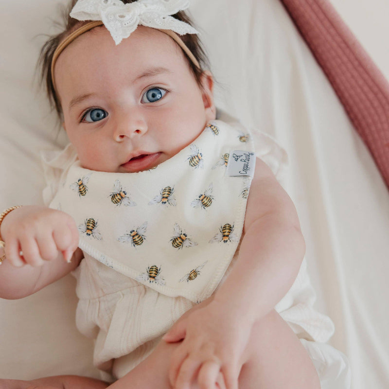 Baby lying in a bassinet wearing the bee print Copper Pearl Catherine bandana bib