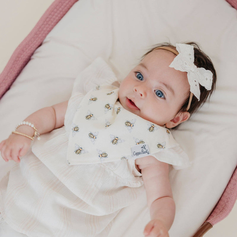 Overhead view of a baby in a bassinet wearing the bee print Copper Pearl Catherine bandana bib