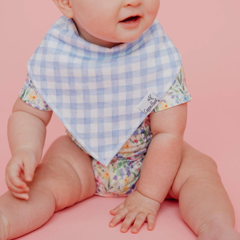 Close-up of the blue gingham Copper Pearl Catherine bandana bib on a seated baby