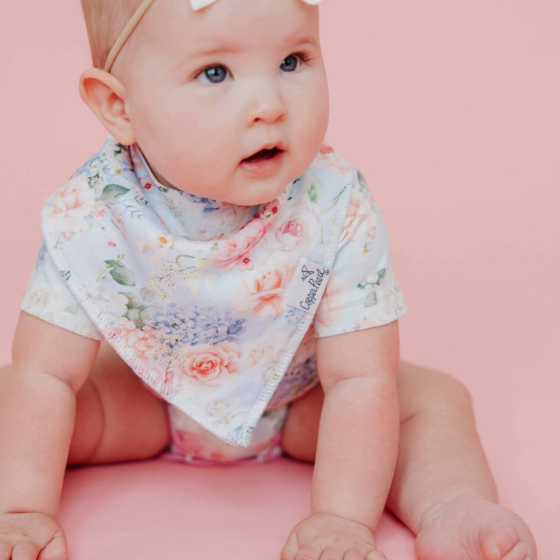Baby on a pink background wearing a floral Copper Pearl Genevieve bandana bib