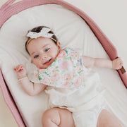 Baby lying in a bassinet wearing the pink rose Copper Pearl Genevieve bandana bib