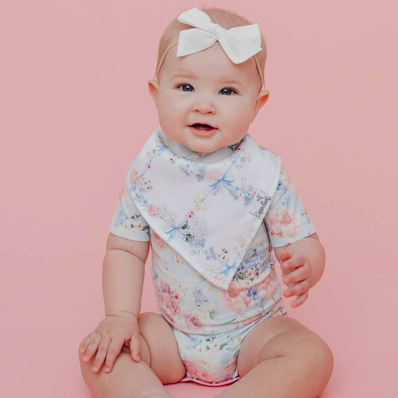 Baby sitting upright on a pink background in a Copper Pearl Genevieve bandana bib