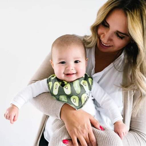 Woman holding a baby wearing an avocado-themed bib against a white background