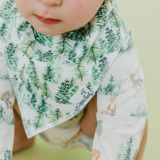 Baby wearing a bib with forest design on a plain background