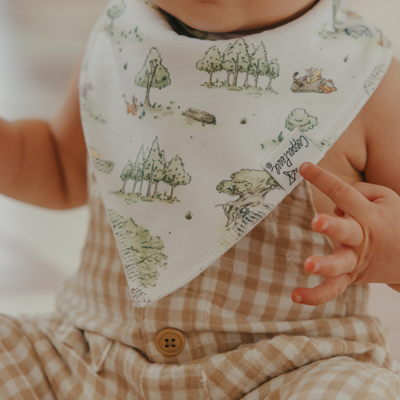 Close-up of a Copper Pearl Hundred Acre Wood bandana bib with a Pooh scenery print