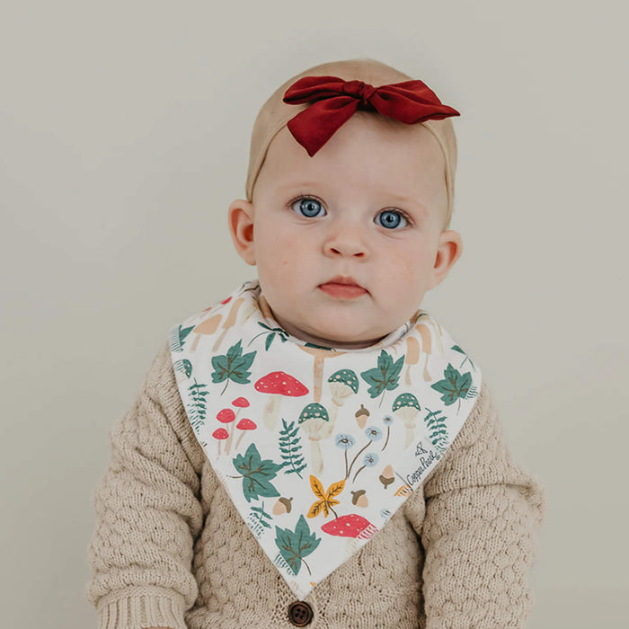 Baby wearing a floral bib and red bow headband against a plain background
