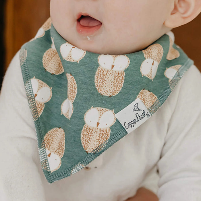 Baby wearing a green bib with owl pattern and 'Copper Pearl' brand tag.