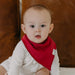 Baby wearing a red bib with a brand logo against a wooden background