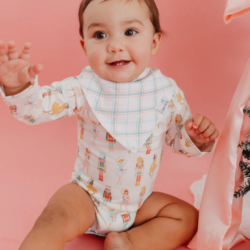 Baby wearing a patterned onesie with a bib, sitting on a pink background