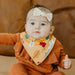 Baby wearing a floral bib and orange outfit with a brown background