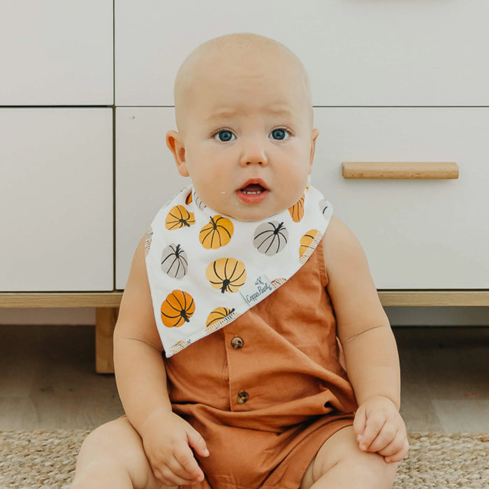 Baby wearing a bib with pumpkin pattern sitting on the floor.