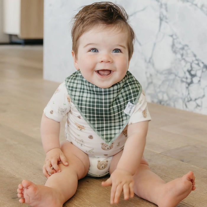 Baby sitting on a wooden floor wearing a green checkered bib.
