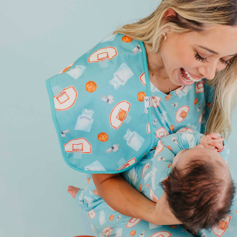Woman smiling down at a baby with the blue basketball Copper Pearl All Star burp cloth on her shoulder