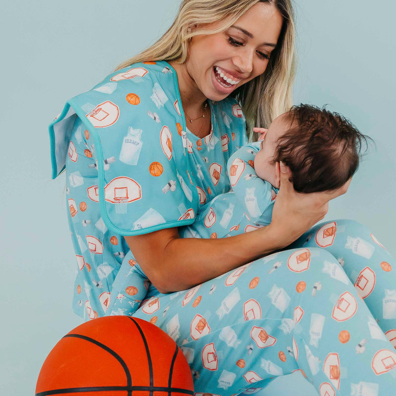 Woman seated beside a basketball holding a baby, with a Copper Pearl All Star burp cloth on her shoulder