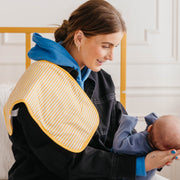 Woman seated holding a baby with the yellow stripe Copper Pearl Dozer burp cloth over her shoulder