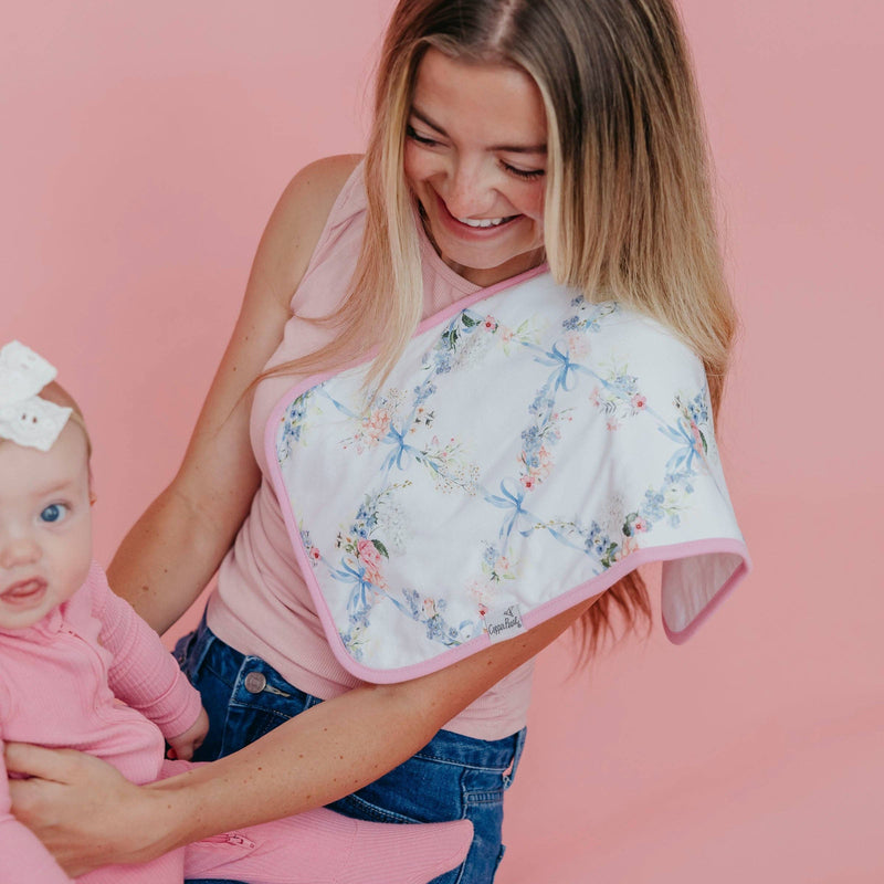 Floral Copper Pearl Genevieve burp cloth draped over a woman's shoulder as she looks down at a baby