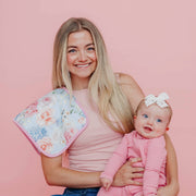 Woman smiling and holding a baby in pink with a Copper Pearl Genevieve burp cloth on her shoulder