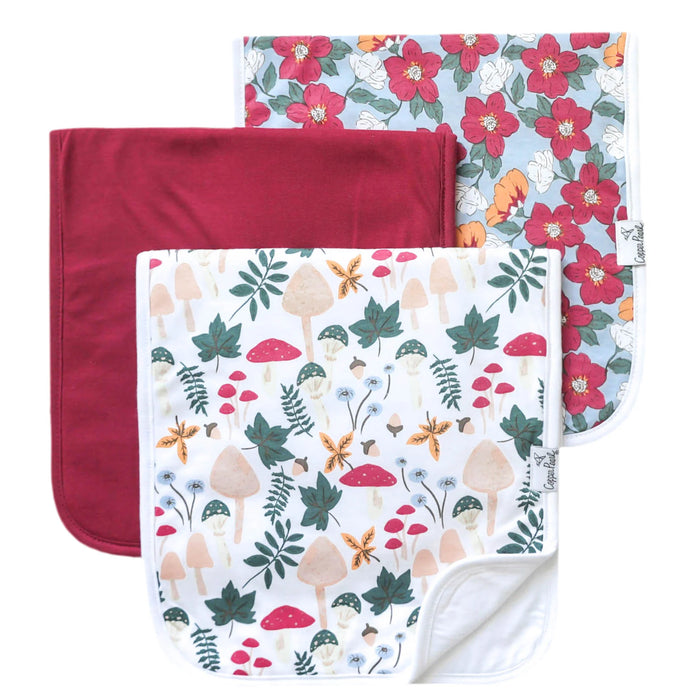 Three Ivy burp cloths laid flat in floral, solid berry, and woodland mushroom prints