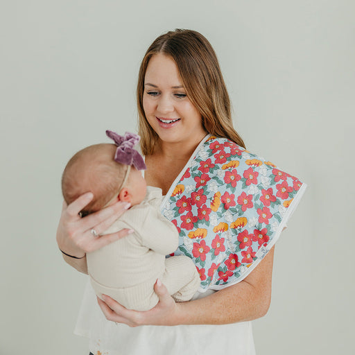 Woman holding a baby wrapped in a floral blanket against a plain background