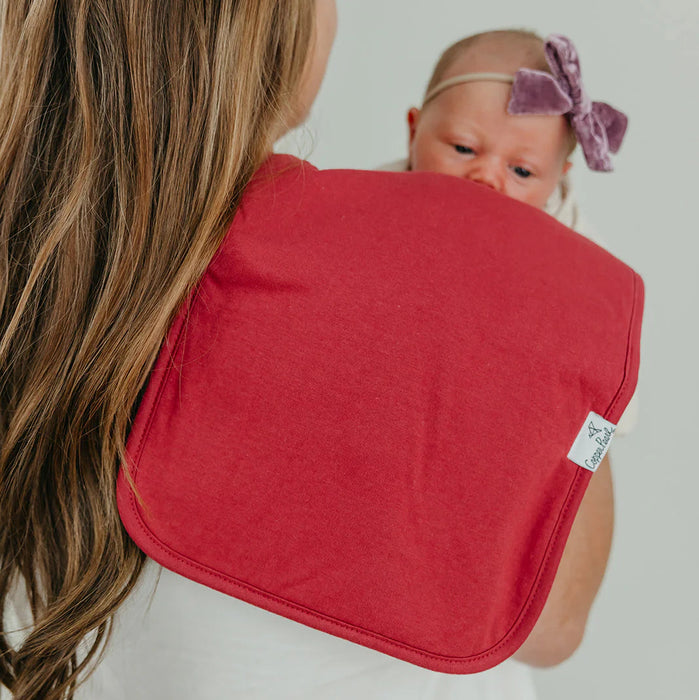 Woman holding a baby wrapped in a red blanket against a plain background
