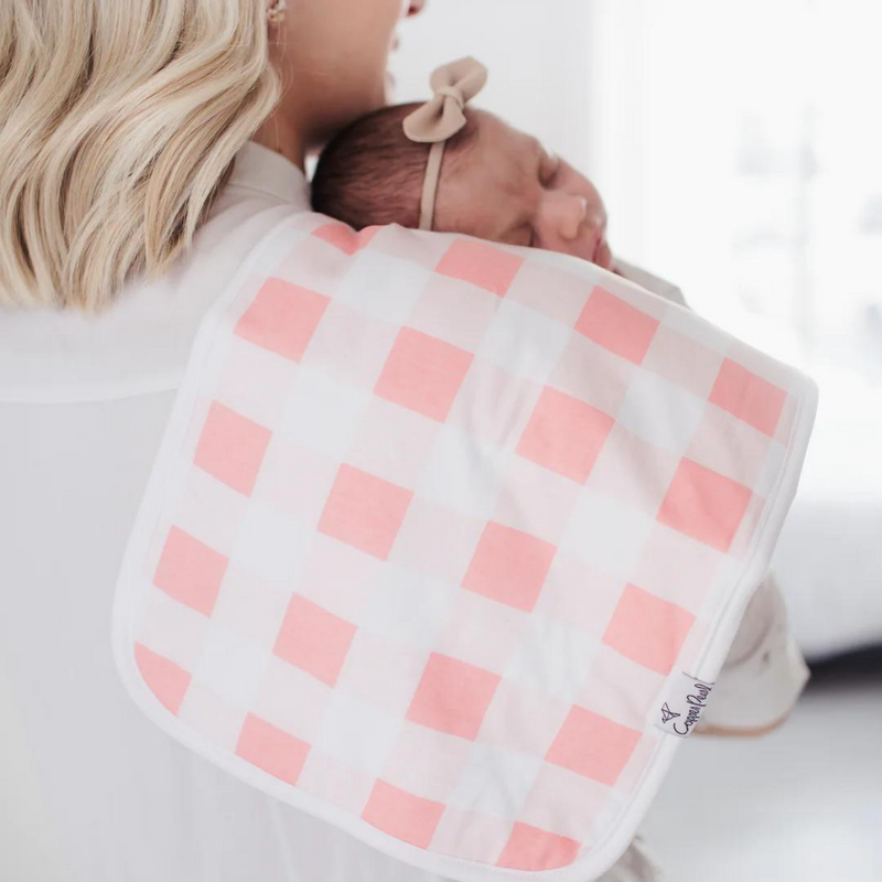 Parent holding baby with a Copper Pearl June burp cloth in pink gingham over the shoulder