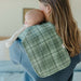 Woman holding a baby wrapped in a green checkered blanket in a bedroom setting.