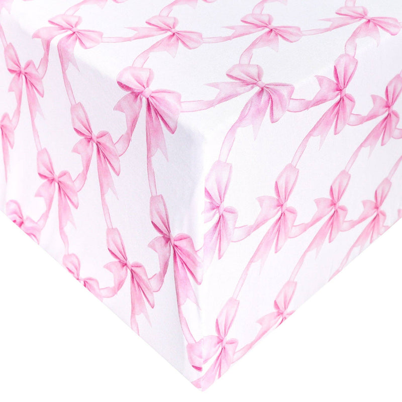 Copper Pearl premium knit fitted crib sheet in Bow My Gosh print, pink bows on white, shown on a mattress corner