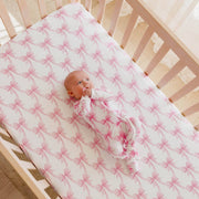 Angled view of a crib fitted with the Copper Pearl Bow My Gosh crib sheet with a baby lying on it