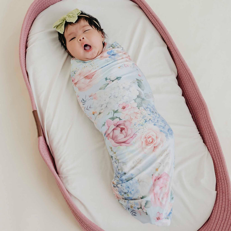 Baby with a bow headband swaddled in the Copper Pearl Genevieve knit swaddle blanket in a pink basket