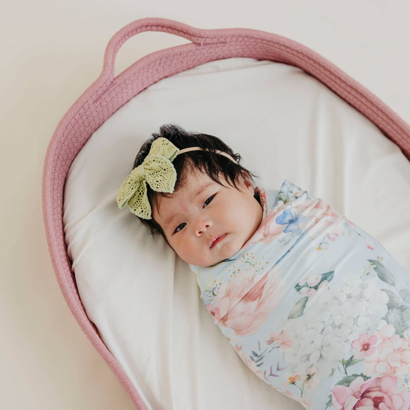 Overhead view of a baby in a pink basket swaddled in the Copper Pearl Genevieve knit swaddle blanket