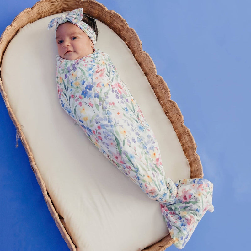 Baby swaddled in the Copper Pearl Josie knit swaddle blanket with a matching headband, lying in a wicker basket