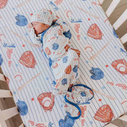 Newborn in a crib wearing the Copper Pearl All Star knotted gown and matching hat on a matching sheet