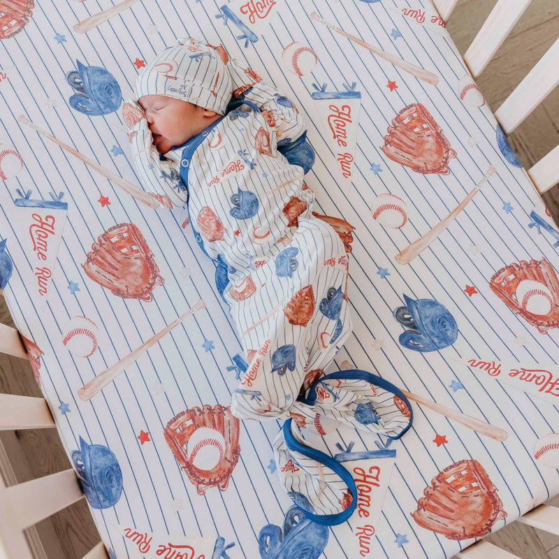 Newborn in a crib wearing the Copper Pearl All Star knotted gown and matching hat on a matching sheet