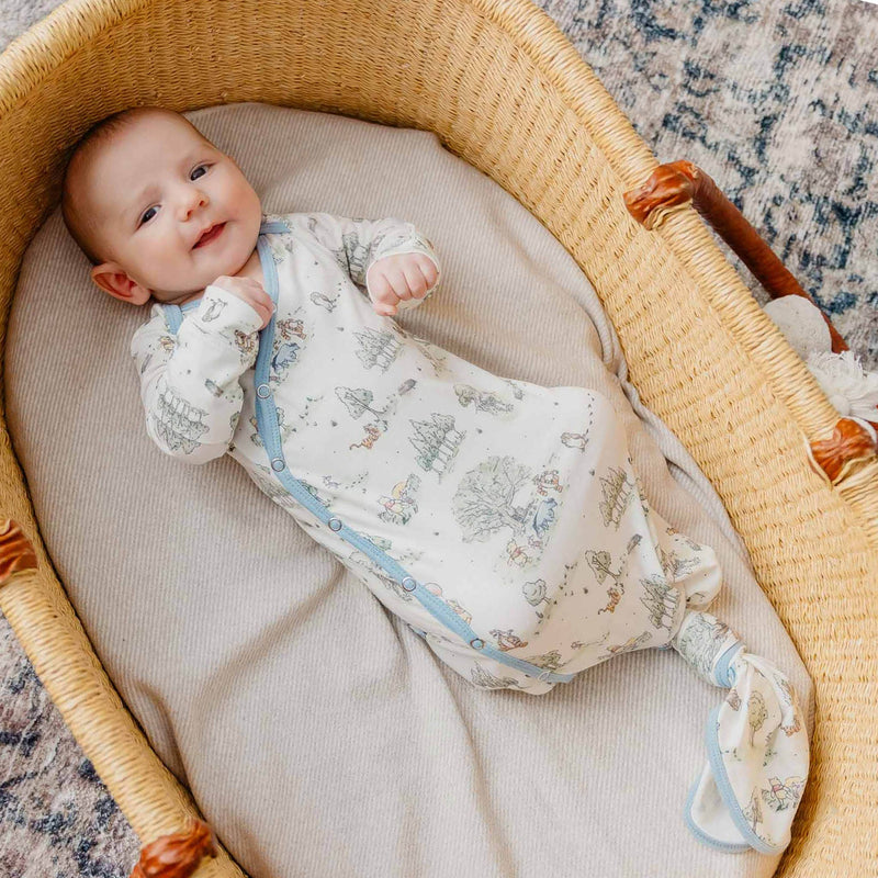 Baby lying in a woven basket wearing the Copper Pearl Hundred Acre Wood newborn knotted gown