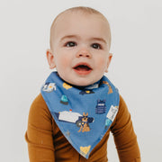 A baby wearing a blue cotton bandana bib with a police-themed print, including a dog, car, and badge, paired with a brown long-sleeve shirt against a light gray background.