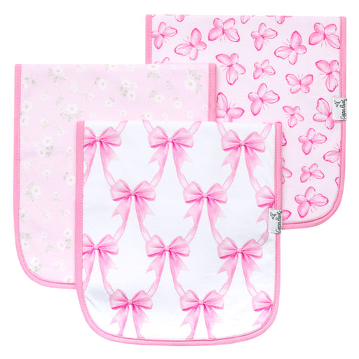 Three square baby bibs with rounded bottom corners, featuring pink and white patterns. The front bib has a repeating pink bow pattern on a white background, the middle bib has a light pink daisy pattern, and the back bib has a pink butterfly pattern.